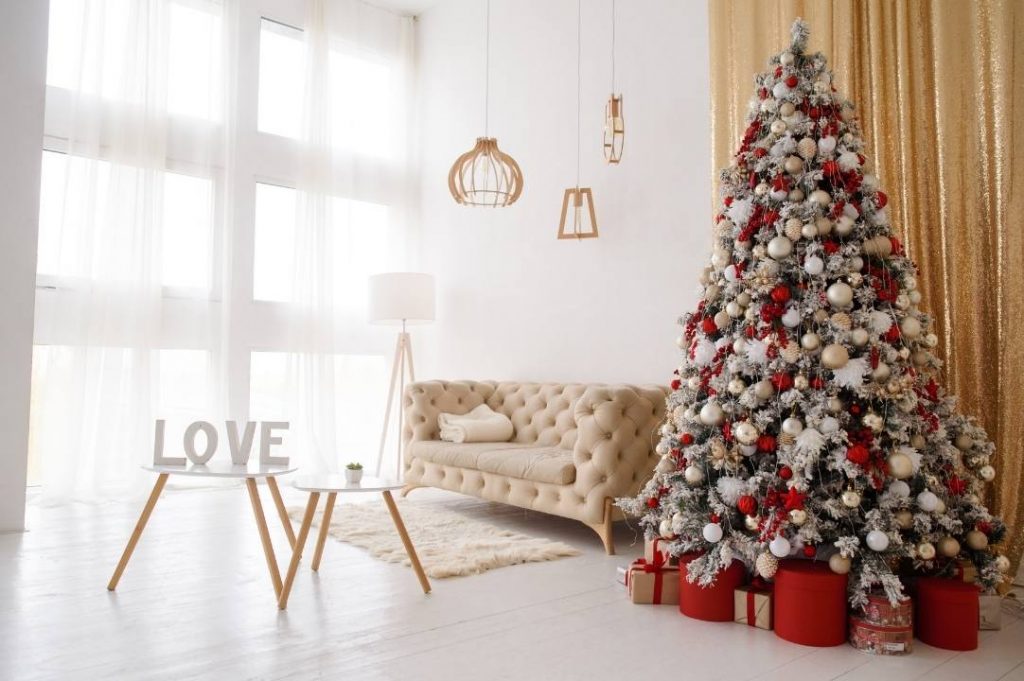 Amuebla tu hogar en Navidad.  Sala de estar con árbol de Navidad plateado y rojo junto a un sofá beige con moqueta peluda.