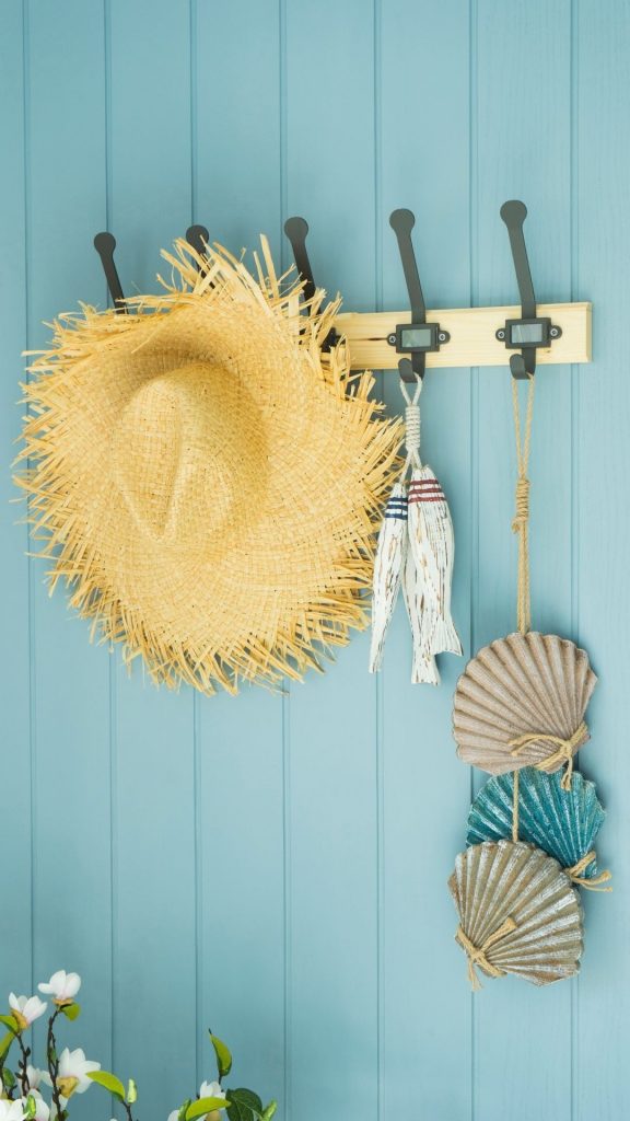Entrada de estilo mediterráneo con revestimientos en azul claro.  Sombrero de paja y conchas colgantes.