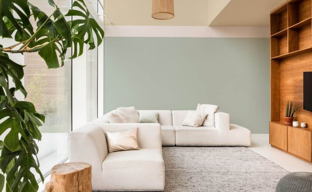 Sala de estar con sofá esquinero blanco, pared verde menta y muebles de madera oscura.