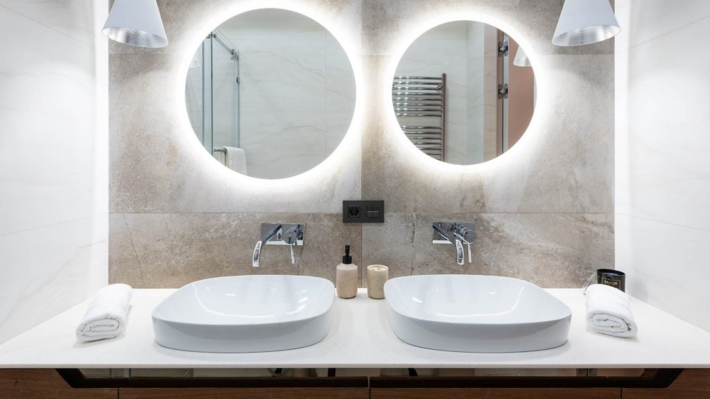 Baño con lavabo doble blanco y dos espejos redondos.